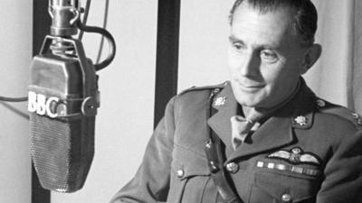 A man in a military uniform looking at a BBC-labelled microphone