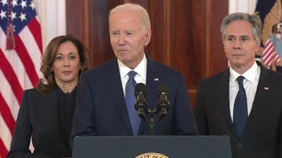 Joe Biden, wearing a navy suit, speaks at a lectern in the White House flanked by Vice President Kamala Harris and Secretary of State Antony Blinken