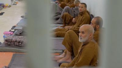 Men sat in a line in a Syrian prison cell