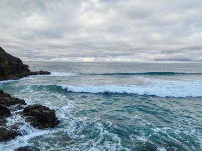 Waves gently crashing against a rocky shoreline with grey cloud above