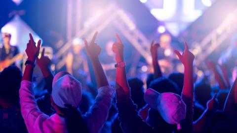 The back of young people's heads can be seen, with their arms raised in the air. 