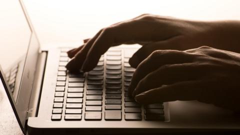 Two hands, darkly lit, using a laptop keyboard.