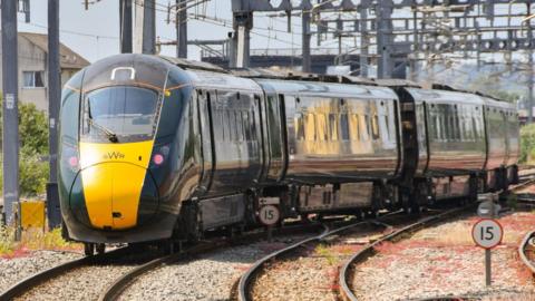 A Great Western Railway train on railway tracks. It is dark green and yellow.