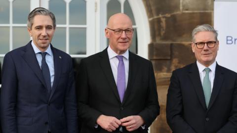 Irish Taoiseach (PM) Simon Harris, First Minister of Scotland John Swinney and British Prime Minister Sir Keir Starmer pose for a photo at the British-Irish Council summit in Edinburgh.  All three men are wearing dark-coloured suits. 