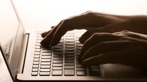 A person's hands can be seen typing on a laptop keyboard. 