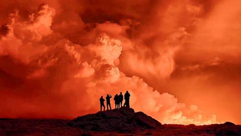 Local residents watch smoke billow as the lava colour the night sky orange from an volcanic eruption on the Reykjanes peninsula 3 km north of Grindavik, western Iceland on December 19, 2023