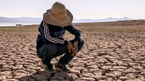 Someone crouching over cracked earth at Al Massira Dam