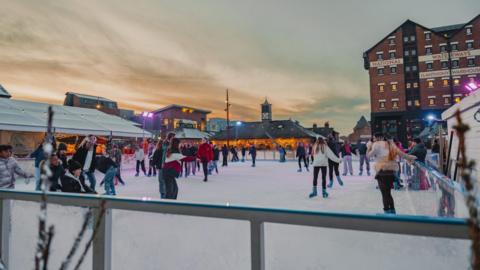 People skating on an ice rink at Gloucester Docks as the sun sets