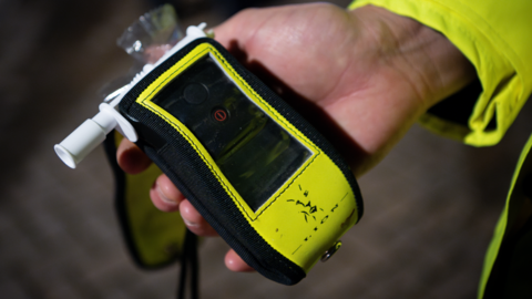 A black and yellow device with a white nozzle on the left hand side, being held in a hand with a yellow sleeve