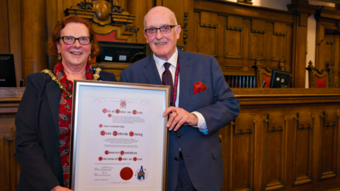 Lord mayor of Stoke-on-Trent Lyn Sharpe poses with Ross Irving. Both are smiling, stood in the council chamber holding a framed certificate which recognises Mr Irving's appointment as the city's honorary custodian.