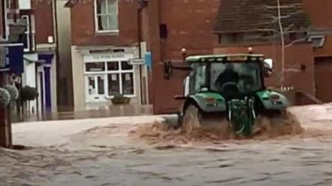 A green tractor in floodwater in a town centre street