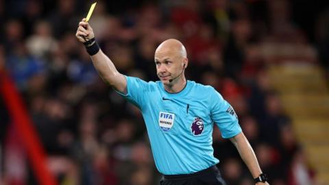 Anthony Taylor raises his arm and holds a yellow card