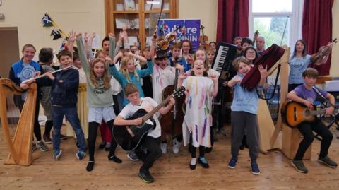 A group of about 20 children holding instruments and pulling faces.