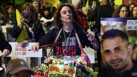 A woman beats a drum as she marched with others who hold flags and placards bearing the faces of hostages