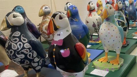 Decorated puffin statues in rows indoors