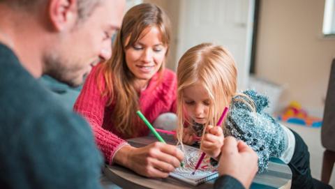 Indoor winter craft activities, a mum, dad and small child drawing and colouring on a table.