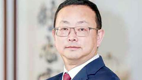 Yang Tengbo smiles at the camera, wearing glasses and a blue suit jacket.
