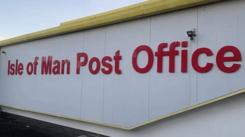 The outside of a one-storey, white flat-roofed industrial unit with Isle of Man Post Office on its wall in large red letters.