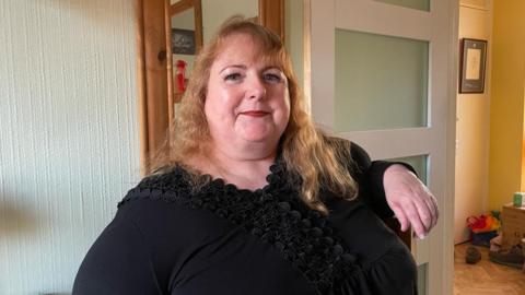 Lisa Braiden wearing a black top and red lipstick smiling at the camera in her home.