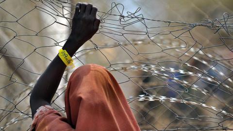 A newly registered Somali refugee supports herself on a chain-link perimeter fence outside a registration and medical aid facility at the Dadaab Internally Displaced People (IDP) camp in eastern Kenya on July 23, 2011