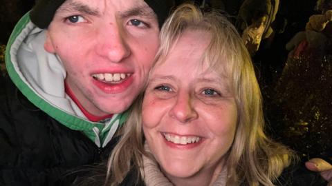 A close-up of the faces of a young man and a woman with shoulder-length hair smiling at the camera.