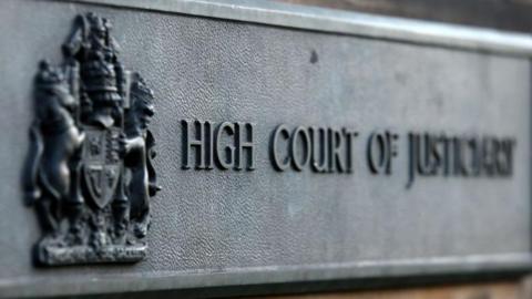 Court sign in grey with an emblem and the words High Court of Justiciary.