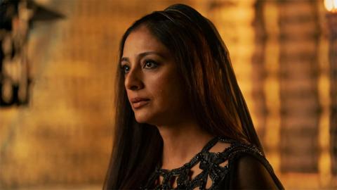 Indian actress Tabu, playing the role of Francesca in Dune, wearing a black outfit and veil on the back of her head. The background is a golden hue.