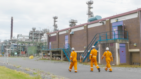 Three workers walk along a path beside the Point of Ayr gas terminal