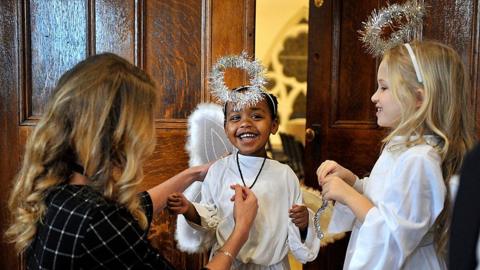 Two primary school children being dressed as angels by a teacher, wearing white robes and tinsel halos