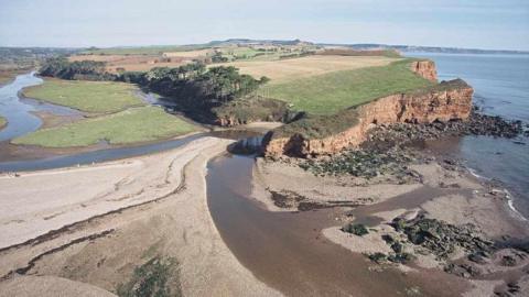 A view from above of Budleigh Salterton, Lower Otter. The cliffs are in shot with the sea to the right of the picture and the sand and grassland to the left.