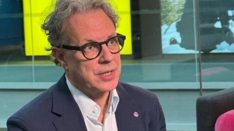 Ian Russell, a man in a dark suit and glasses, looks to the right of the camera while he talks