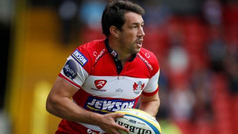 Tom Voyce playing for Gloucester, wearing a red and white shirt and carrying a ball.