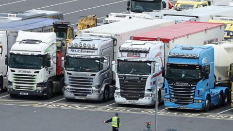 Four lorries in a row, a man in hi vis stands in the foreground, in the parking area of an industrial area