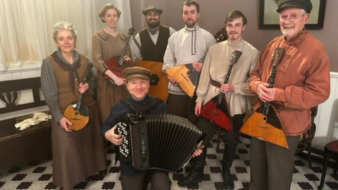 Seven members of the Kalinka Balalaika Orchestra in traditional Eastern European costumes pose with their instruments 