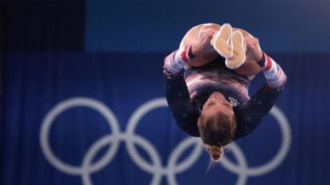 Laura Gallagher in a pike position, while upside down, in a Team GB leotard, backed by the Olympic Rings