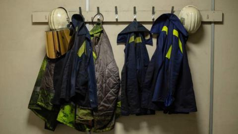 Day-glow overalls and helmets used by steelworkers hung on coat hooks