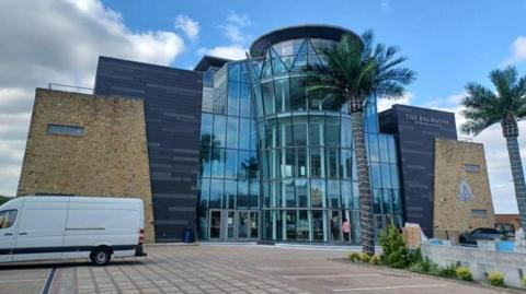 Exterior of Balmayna, which has a four-floor glass front topped by a crown and palm trees in the car park outside