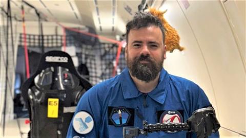 Dr Gilles Bailet wearing a blue flight suit in a zero gravity aircraft. 