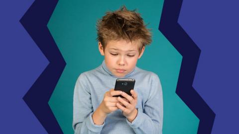 A young boy staring at a smart phone that he is holding in his hand.