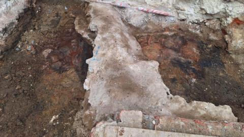 An archaeologist's close up photo of a medieval hearth. A lighter stone structure is pictured in between darker earth, forming part of a dig at Oriel College in Oxford.