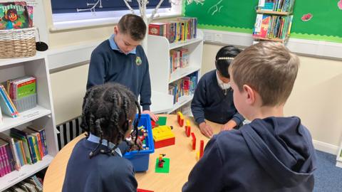 Four primary school children stand around a table playing with lego.