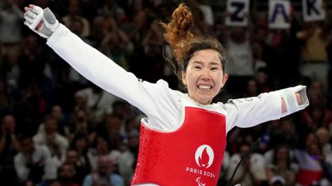 Zakia Khudadadi lifts her arms wide in celebration after winning a Paralympic bronze medal in Para-taekwondo