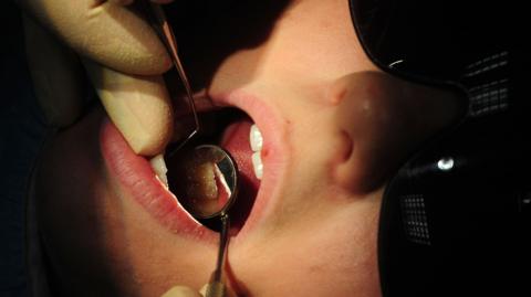 Someone receiving dental treatment with instruments in their mouth and wearing a black eye mask.