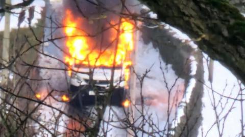 A police van on fire on a snow-covered road.