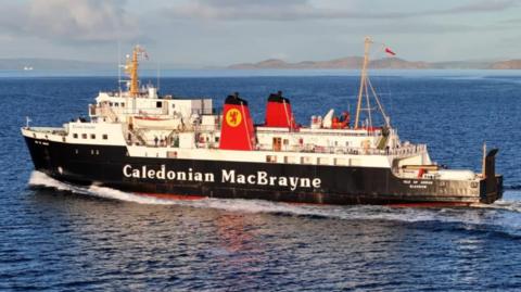 A black and white ship with red funnels, sailing from right to left, with hills in the background