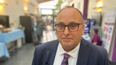 Ifti Majid, chief executive of Nottinghamshire Healthcare NHS Foundation Trust, is pictured wearing black-rimmed glasses, a dark blue suit, white shirt and tie