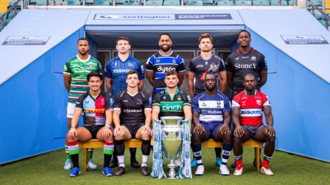 A player from each Premiership rugby club sitting and standing behind the Premiership trophy