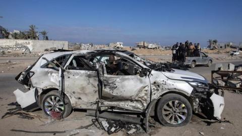 The wreckage of a car seen following an Israeli strike in southern Gaza. The car is white but partially burned-out. It's roof is caved in, it is missing its windows, and its tyres are flat. 