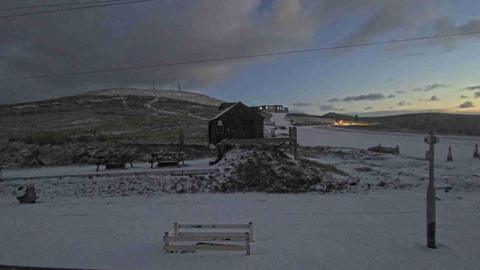 White snow has fallen on a hillside, you can see a wooden hut. The sun rises too.