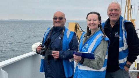 Left to right are Ian Boreham, Amelia Hersant and Terry Carne on board the ferry. All are wearing blue and grey lifejackets